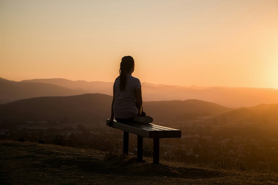 woman sitting on bench overlooking a town in a valley, self-care secrets